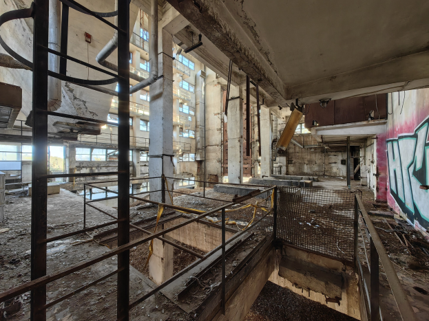 Verlassene Gebäudeinnenseite mit Graffiti-beschmierten Wänden, bröckelnder Struktur, kaputten Fenstern, Geländern, Polen, Rohren und anderem Schutt; Wasserzeichen unten.