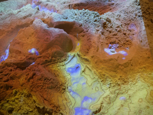 Nahaufnahme einer detaillierten 3D-Karte einer Wüstenlandschaft, die sandfarbene Berge, Täler und Grate unter heller Beleuchtung zeigt.