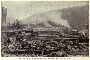 Schwarzes und weißes Foto einer Stadt nach einer Katastrophe am 5. Juni 1892, das Gebäude, Strommasten, Rauch und einen Hügel im Hintergrund zeigt, mit Text unten.