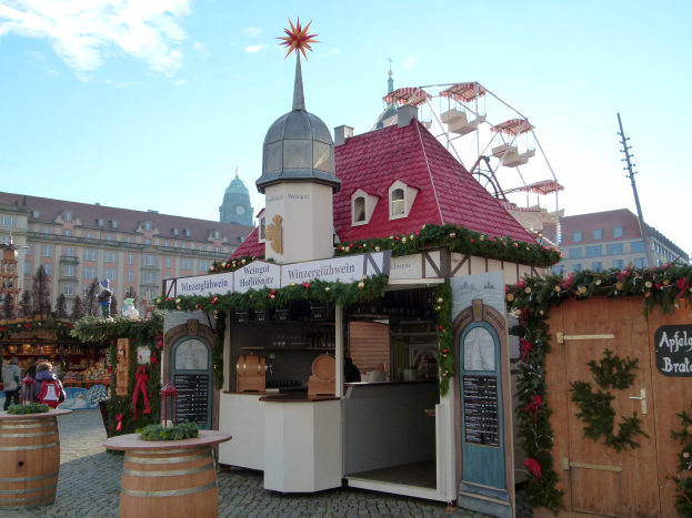 Kleines rotes Dachgebäude mit einem Riesenrad davor, umgeben von Festdekorationen und Menschen bei einem Oktoberfest-Event in München, Deutschland.