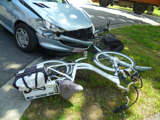 Auto am Straßenrand mit einem Fahrrad auf dem Gras in der Nähe, Bäume und ein klarer blauer Himmel im Hintergrund.