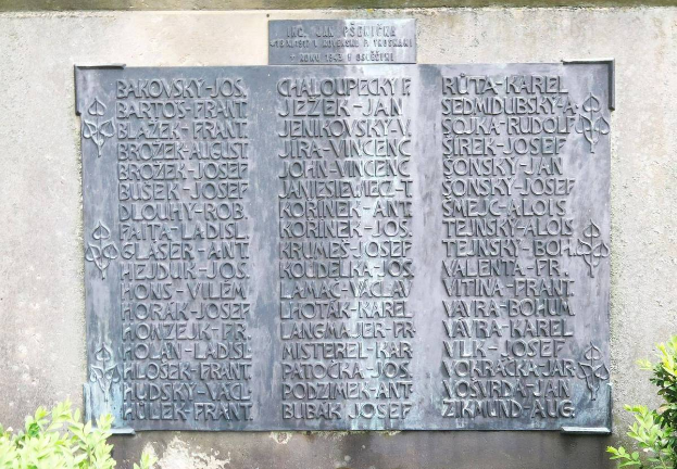 Ein Steinplakette an einer Wand mit eingravierten Text, umgeben von Pflanzen unten, wahrscheinlich ein Holocaust-Mahnmal.