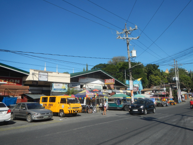 Eine belebte Straße mit Autos, Motorrädern, Fußgängern, Zelten, Gebäuden, Strommasten, Bäumen und einem klaren blauen Himmel.