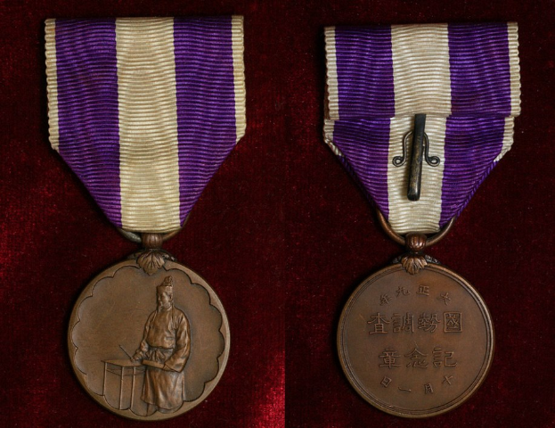 Zwei Medaillen mit lila und weißen Bändern, mit eingravierter Schrift, auf einer maronenfarbenen Oberfläche.