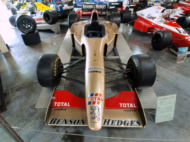 Rennwagen in einem Museums Setting mit einem Metallzaun links und einer Informationswand im Hintergrund.