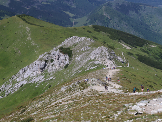 Gruppe von Menschen beim Wandern auf einer grasigen, steinigen Bergseite mit einem klaren Himmel im Hintergrund.