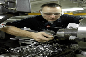 Ein Monteur trägt einen Schutzhelm und bedient eine Maschine in einer gut beleuchteten Fabrikumgebung.