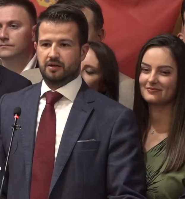 Ein Mann im Anzug spricht an einem Pult mit einem Mikrofon zu einer Menge hinter einem Banner, wahrscheinlich über ein gouvernementales Verbot von sozialen Medien.