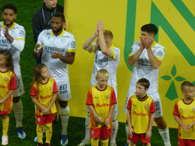 Eine Gruppe von Füßballspielern in Uniform klatscht auf einem Ligue-1-Feld in celebration, mit einem "Ligue-1"-Schild im Hintergrund.