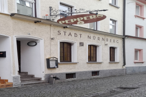 Gebäude mit einer "Stadt Nurnberg"-Aufschrift, Fenstern, einer Tür, einer Treppe und einem Müllcontainer im Vordergrund.
