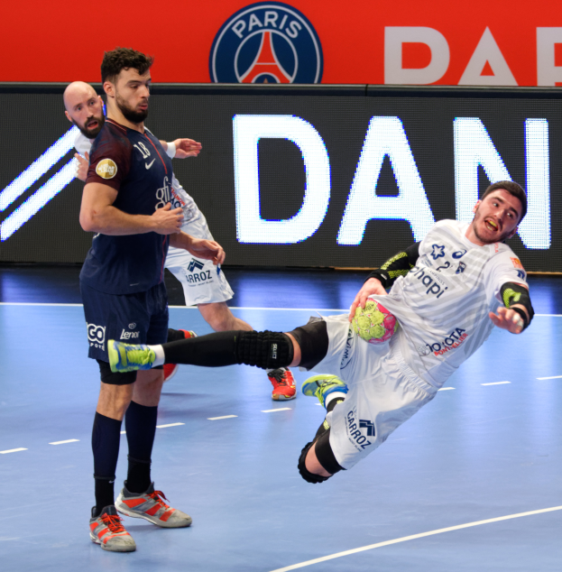 Eine Gruppe von Männern spielt Handball auf einem Platz, einer hält den Ball, im Hintergrund ein Paris Saint-Germain Futsal-Team-Schild.