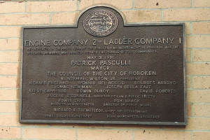 Schwarzes rechteckiges Schild an einer Backsteinwand mit weißer, fetter, zentrierter Schrift, die 'Feuerwehrkompanie 2 Leiterkompanie' liest.