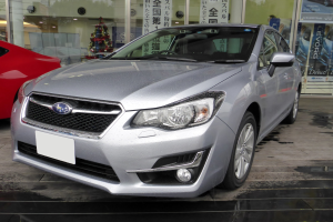 Silberner Wagen vor einem roten Auto mit einer Glaswand im Hintergrund, die einen Weihnachtsbaum, Lichter und Plakate von Autos zeigt.