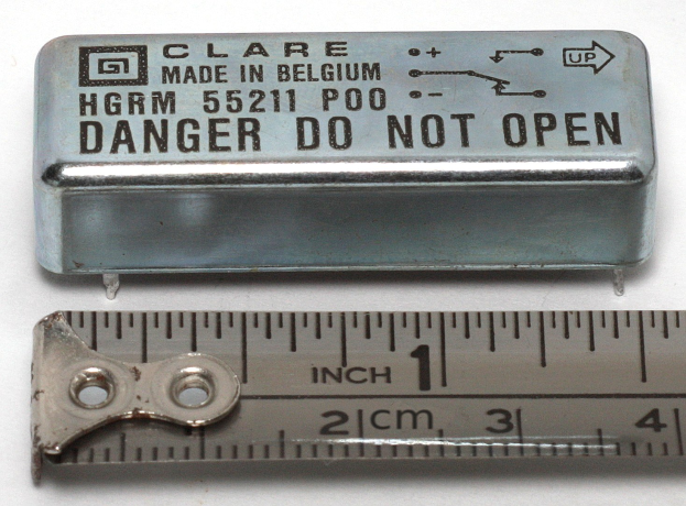 Metallbox mit Aufschrift "Danger Do Not Open" neben einer Messlatte auf einer weißen Oberfläche.