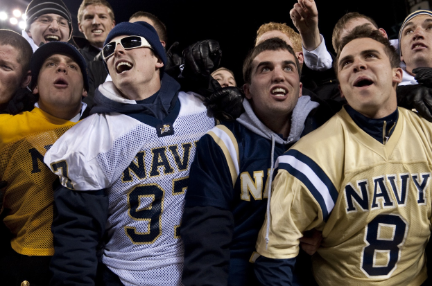 Fans der Navy-Fußballmannschaft jubeln während eines Spiels unter Flutlicht.