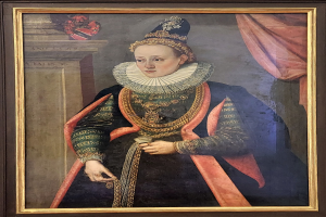Porträt der Queen Elizabeth I. von England in königlicher Kleidung mit Krone und Tiara, das Haar zu einem Knoten gebunden, mit einem würdevollen Gesichtsausdruck zur Seite blickend, in einem Rahmen an der Wand gehängt.