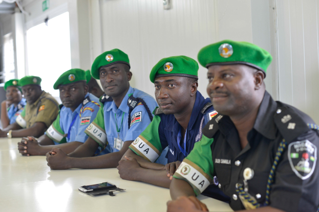Gruppe von Polizeibeamten sitzt an einem Tisch während einer Schulung, mit Mobiltelefonen und anderen Gegenständen auf dem Tisch, in einem Raum mit Fenstern und Deckenbeleuchtung.