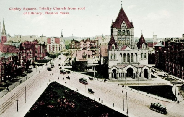 Schwarz-weiß-Fotografie von Copley Square in Boston, die Trinity Church und umliegende Gebäude von der Dachterrasse der Bibliothek aus zeigt, mit Straßenlaternen, Fahrzeugen, Fußgängern, Bäumen und Himmel im Bild.