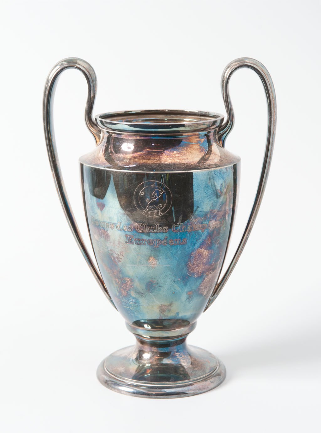 Der UEFA-Champions-League-Pokal, ein stählerner Becher mit zwei Griffen und einem blauen und silbernen Farbschema, der mit "UEFA Champions League" gegen einen weißen Hintergrund eingraviert ist.