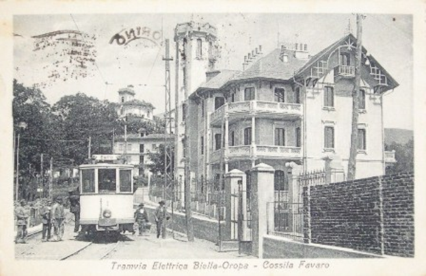 Ein altes Schwarz-Weiß-Foto einer Straßenbahn auf Schienen, umgeben von Gebäuden, Bäumen, Polen und Menschen, mit Text unten.
