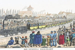 Eine Gruppe von Menschen steht um einen Zug auf einem Gleis, einige sitzen im Zug und andere stehen draußen, in der Nähe von Gebäuden und Bäumen, mit Text 'Ludwigs-Eisenbahn, der erste Bahnhof in Deutschland' unten.