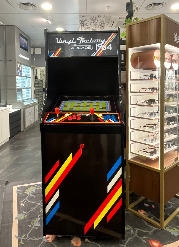 Vintage-Arcade-Automat in einem Laden im Retro-Stil mit Gläsern auf einem Gestell, Schränken, einem Fernseher und Deckenlampen im Hintergrund.