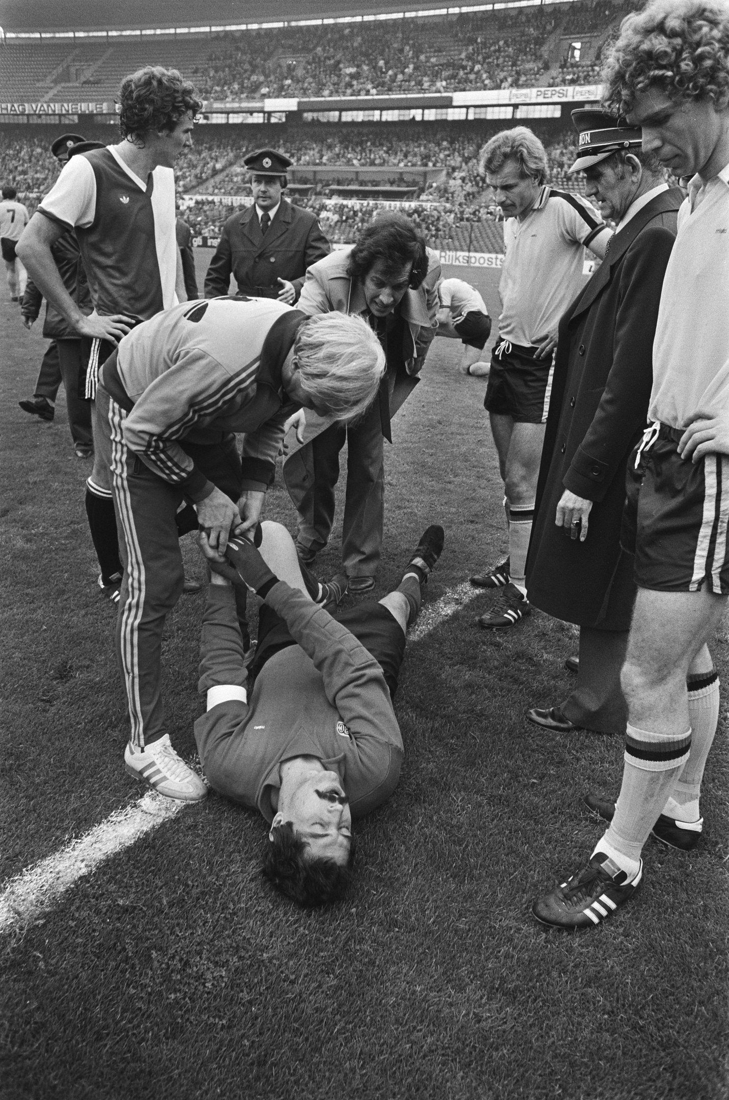 Schwarzes und weißes Bild von Fußballspielern und einer Menge in einem Stadion um einen verletzten Spieler auf dem Boden herum.