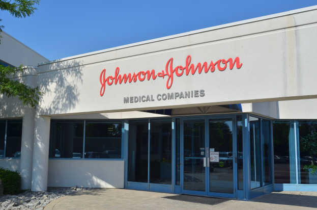 Außenansicht des Johnson & Johnson Medical Companies-Gebäudes mit Glaswänden, Text an der Fassade, Steinen, Pflanzen und einem Baum vor einem klaren blauen Himmel.