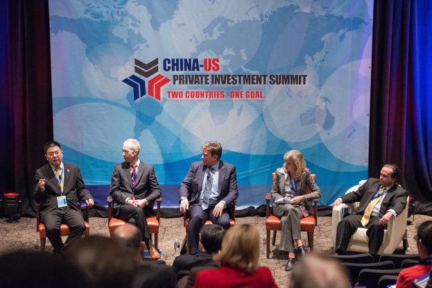 Eine Gruppe von Menschen, die auf Stühlen sitzen und einem Bildschirm mit Text und einer Karte zugewandt sind, mit Vorhängen im Hintergrund, was auf einen China-US-Privatinvestment-Gipfel hinweist.