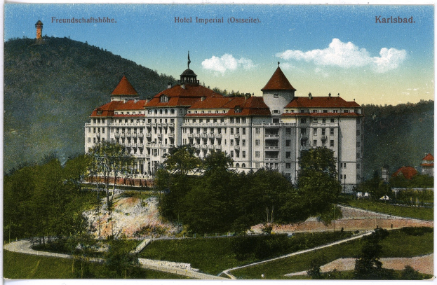 Alte Ansichtskarte des Hotel Imperial in Karlsbad, Deutschland, zeigt ein großes Gebäude mit Fenstern, umgeben von Bäumen, Pflanzen, Gras, einem Weg, einer Baumgruppe, Hügeln und einem bewölkten Himmel, mit Text oben.