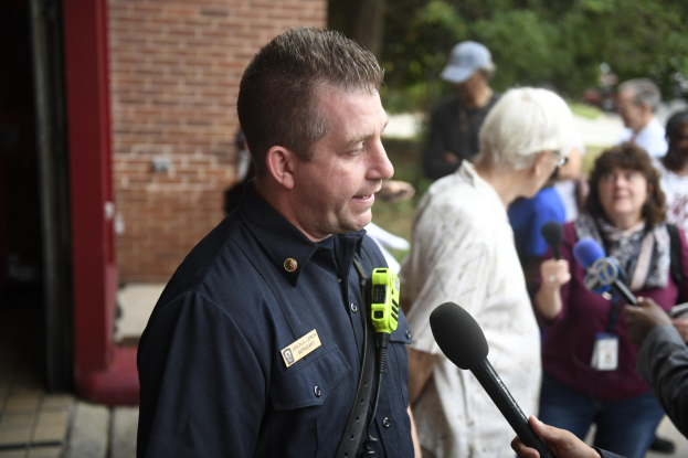 Ein Polizeibeamter in Uniform, der zu einer Gruppe von Menschen spricht, mit Bäumen und einem Gebäude im Hintergrund.