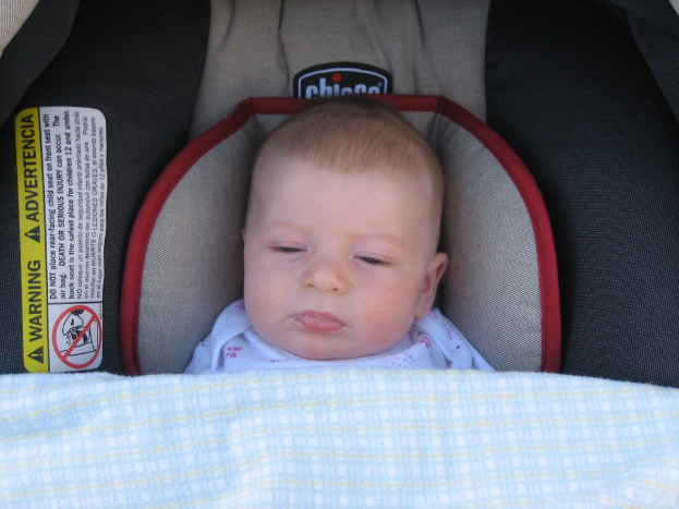 Baby unter einer Wiege liegend mit einem Warnaufkleber auf der linken Seite.