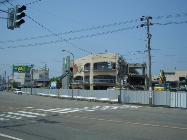 Eine Stadtstraße mit fahrenden Fahrzeugen, Strommasten, Ampeln und einem Gebäude in der Ferne.