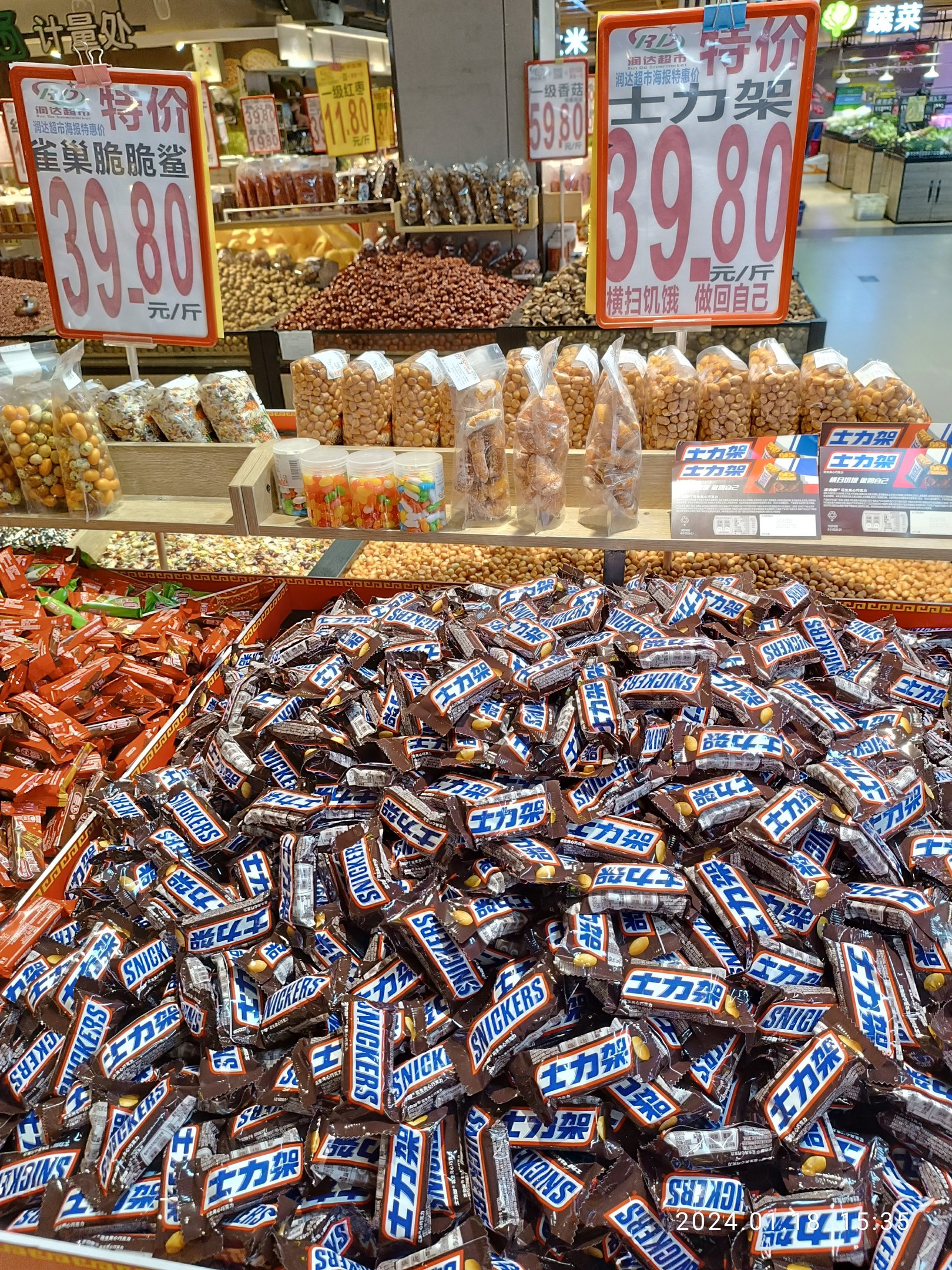 Vitrine mit verschiedenen Arten von Süßigkeiten, einschließlich Snickers-Riegeln, in einem Geschäft mit Lebensmitteln auf Regalen und Hintergrund-Elementen.
