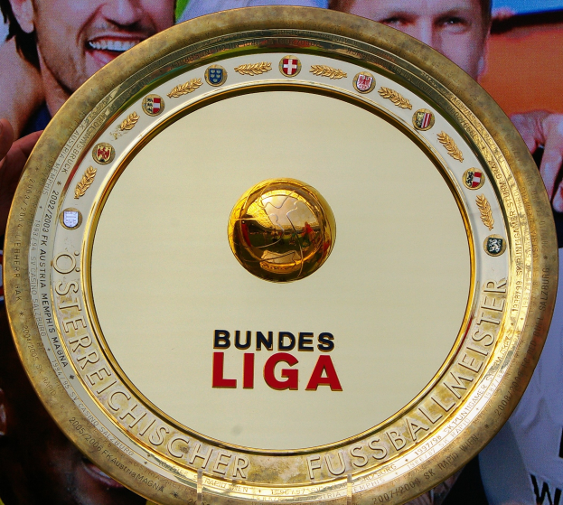 Ein Mann hält einen goldenen Schild mit der Aufschrift "Bundesliga", im Hintergrund eine Fahne mit drei Personen