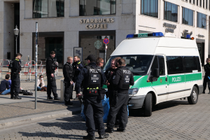 Eine Gruppe von Polizeibeamten steht vor einem Starbucks-Café, rechts ein Van und links ein paar Menschen; im Hintergrund sind ein Gebäude, ein Schild, ein Laternenmast und ein Zaun zu sehen.
