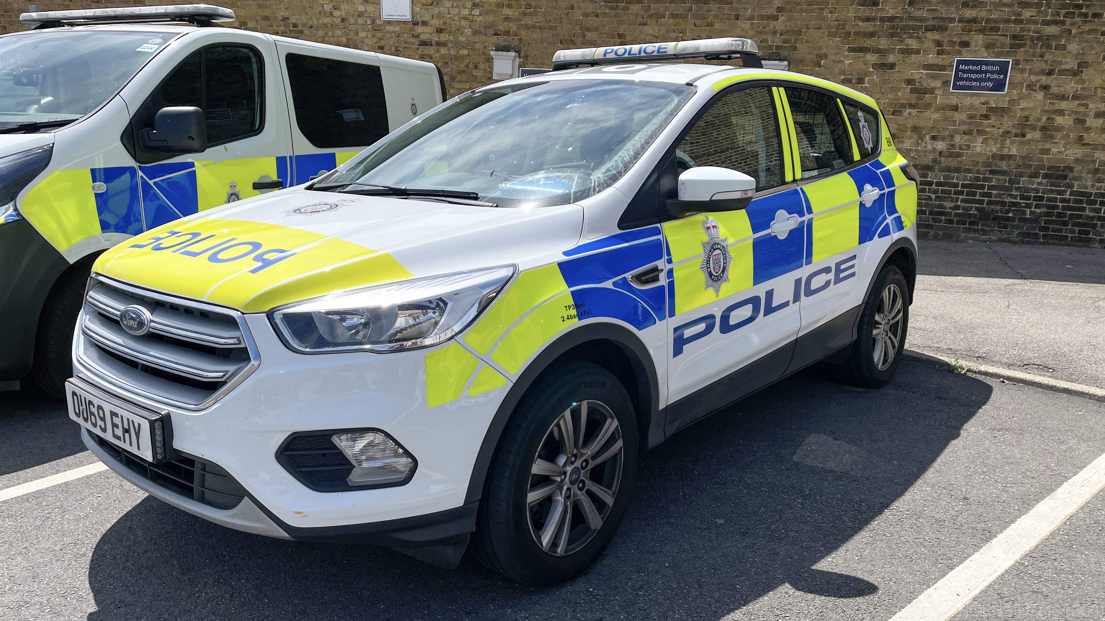 Zwei Polizeiwagen nebeneinander auf einem Parkplatz mit einer Wandtafel im Hintergrund.
