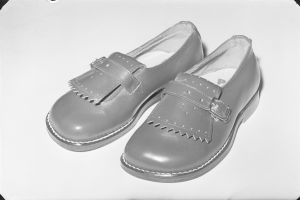 Schwarzes und weißes Foto eines Paares klassischer schwarzer Lederschuhe mit gerundeter Spitze und niedrigem Absatz auf einer weißen Oberfläche, mit glänzender Oberseite und strukturierter Sohle.