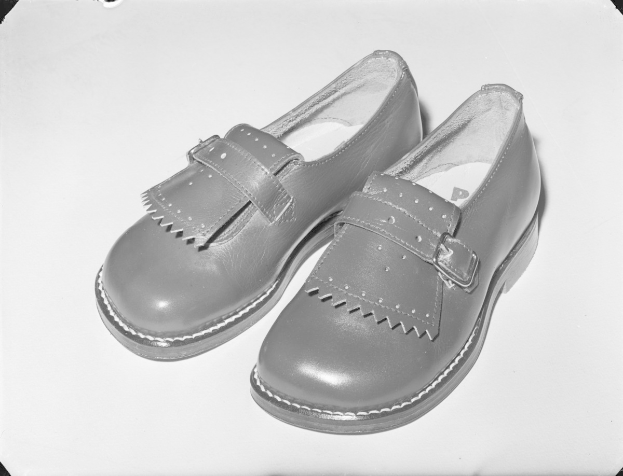 Schwarzes und weißes Foto eines Paares klassischer schwarzer Lederschuhe mit gerundeter Spitze und niedrigem Absatz auf einer weißen Oberfläche, mit glänzender Oberseite und strukturierter Sohle.