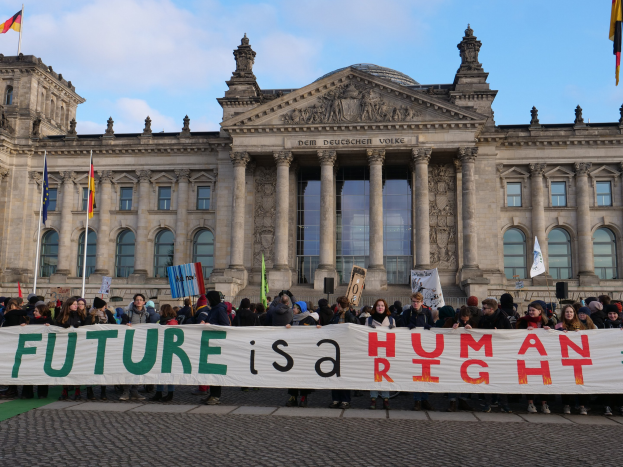 Eine Gruppe von Menschen hält ein Transparent mit der Aufschrift "Zukunft ist ein Menschenrecht" vor dem Reichstaggebäude in Berlin, Deutschland, mit dem Himmel im Hintergrund.
