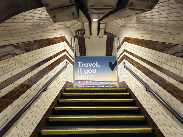 Eine Treppe in einer U-Bahn-Station mit einem 'Reise, wenn du wagst'-Schild oben, flankiert von Geländern und sichtbaren Stationwänden.