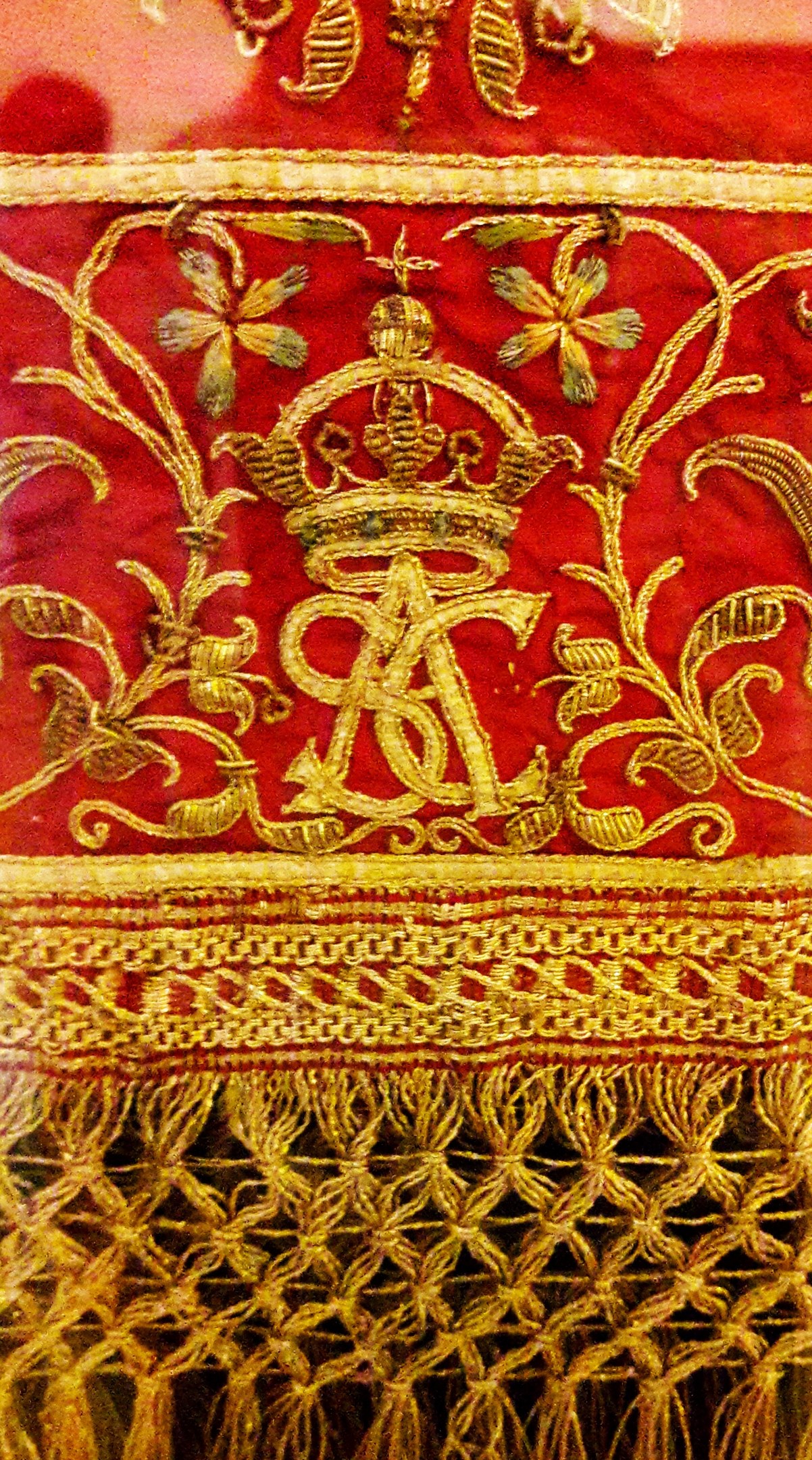 Nahaufnahme eines roten und goldenen Tuchs mit einer Krone und aufwändiger Goldstickerei, das einen luxuriösen und königlichen Eindruck vermittelt.