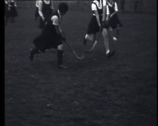Schwarzes und weißes Foto von jungen Mädchen, die auf einem Feld Hockey spielen, jede hält einen Hockeystock in der Hand.