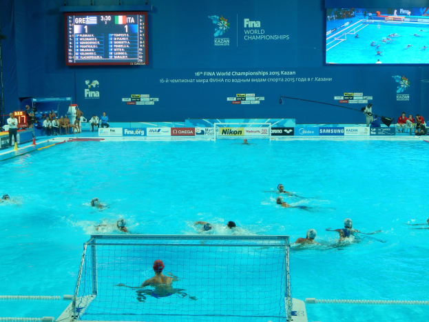 Wasserballspieler bei einem Pool-Wettkampf während der FINA-Weltmeisterschaften 2016 in Kazan, mit Zuschauern auf der linken Seite und einem Scoreboard im Hintergrund.