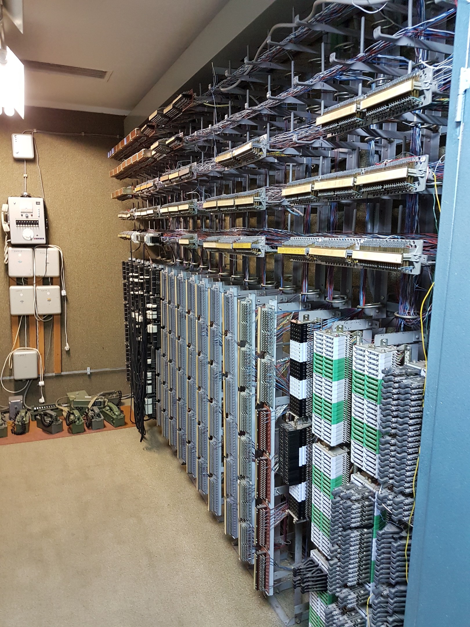 Ein unordentlicher Rechenzentrumsraum mit zahlreichen Servern, Kabeln und elektronischen Geräten auf dem Boden und einer Wand auf der linken Seite.