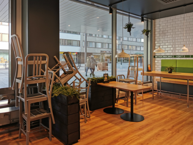 Ein Restaurant in Berlin mit Holztischen und -stühlen vor einem großen Fenster, das eine Außenansicht von Fußgängern, Gebäuden und städtischen Elementen zeigt.