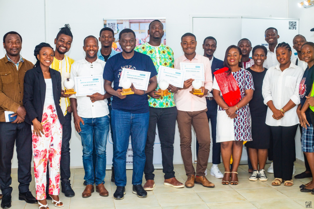 Eine Gruppe strahlender Menschen mit Urkunden, die neben einem Tisch mit Gegenständen in einem Raum mit Brettern und einem Plakat stehen, feiern die Gewinner der WIK Awards 2019.