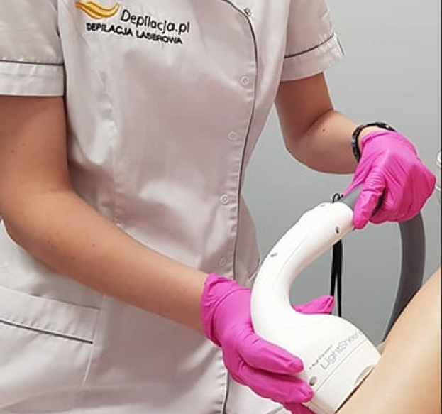 Eine Frau in einem weißen Hemd und pinken Handschuhen verwendet eine weiße Laser-Haarterminationsmaschine auf ihrer Haut, während sie vor einer Wand steht.