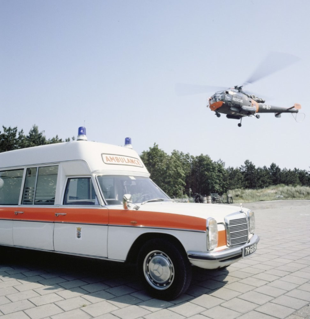 Notarztwagen vor einem Hubschrauber mit Bäumen und einem klaren blauen Himmel im Hintergrund.