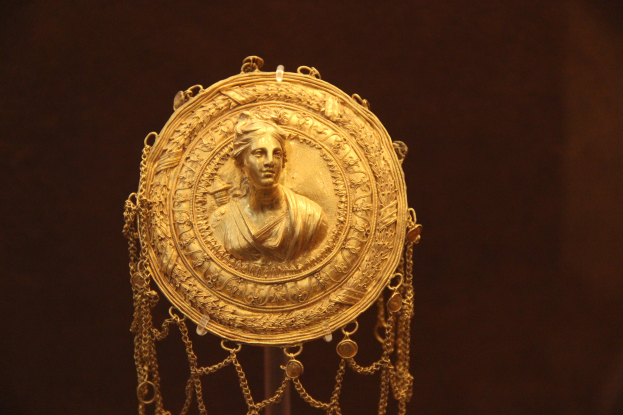 Goldene Medaille mit einer Frauengesicht, vor einem dunklen Hintergrund, mit aufwendigen und luxuriösen Details.